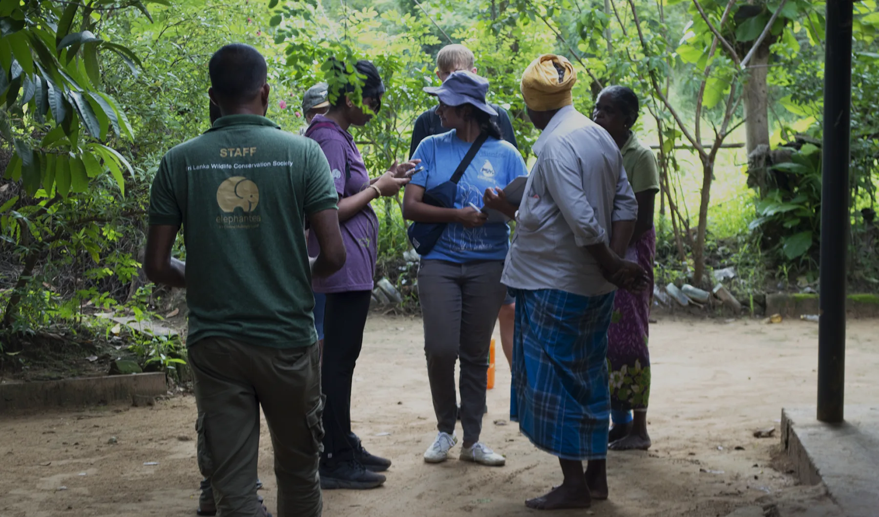 Volunteers and SLWCS staff meeting villagers in a home garden